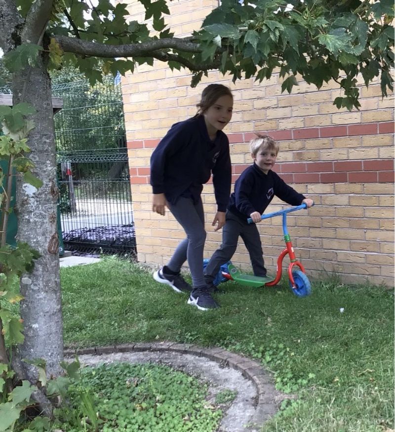 one child on scooter with older child supporting