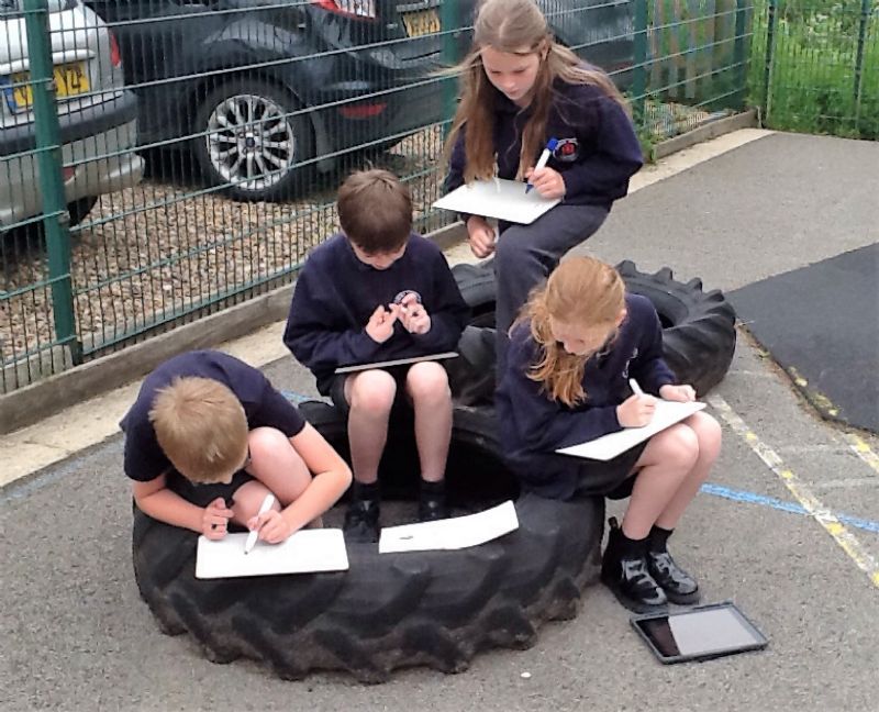 Four children sitting on a tyre working out maths questions 
